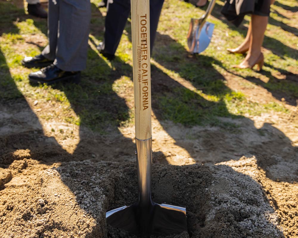 A shovel in the dirt with a logo engraved on the handle.