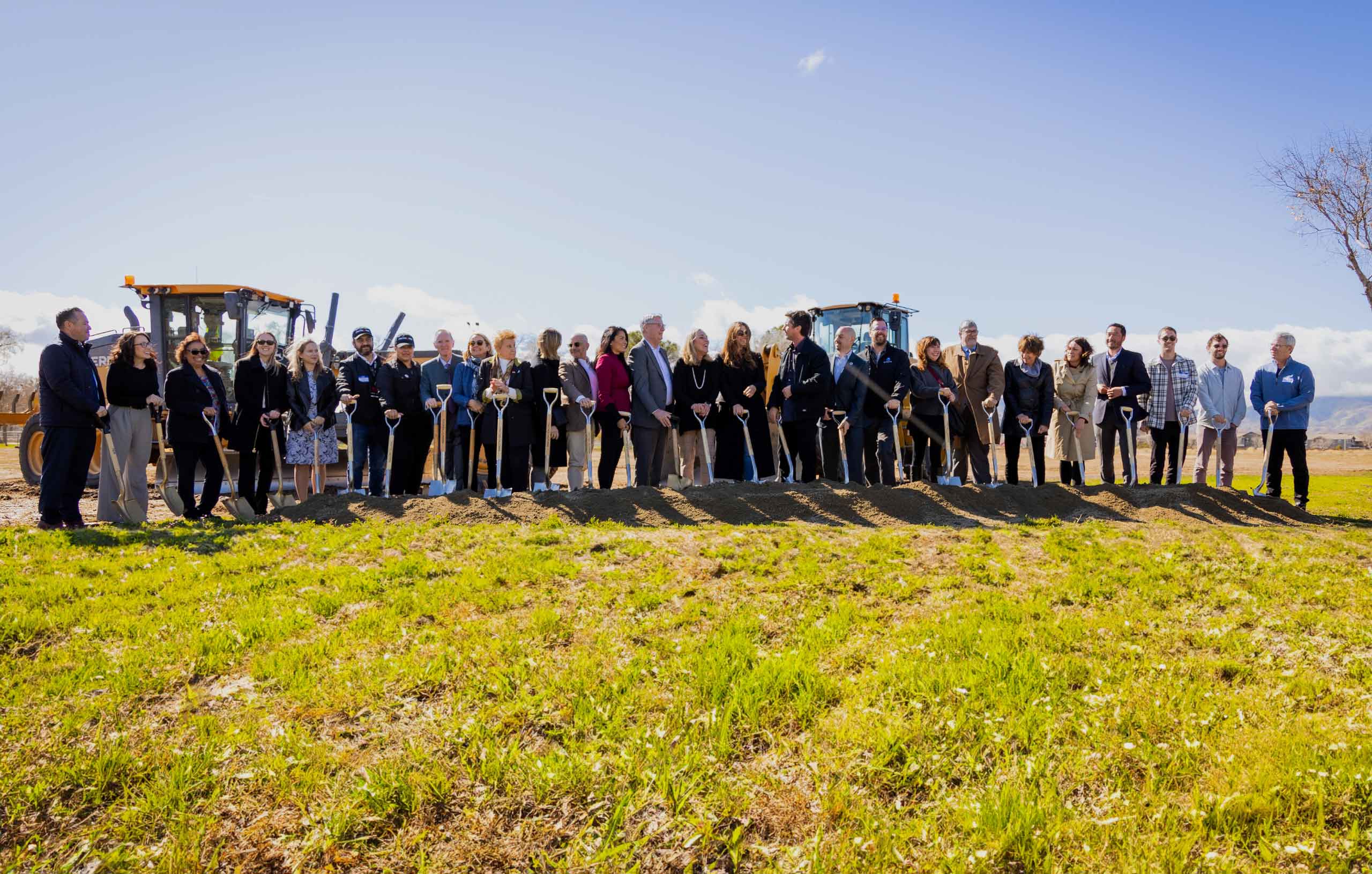 A large group of people standing on grass with shovels.