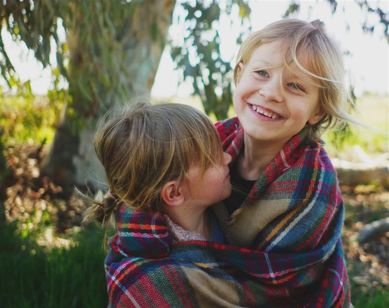 Two siblings smiling and wrapped in a blanket, symbolizing Together California Foster Care's village for brothers and sisters.